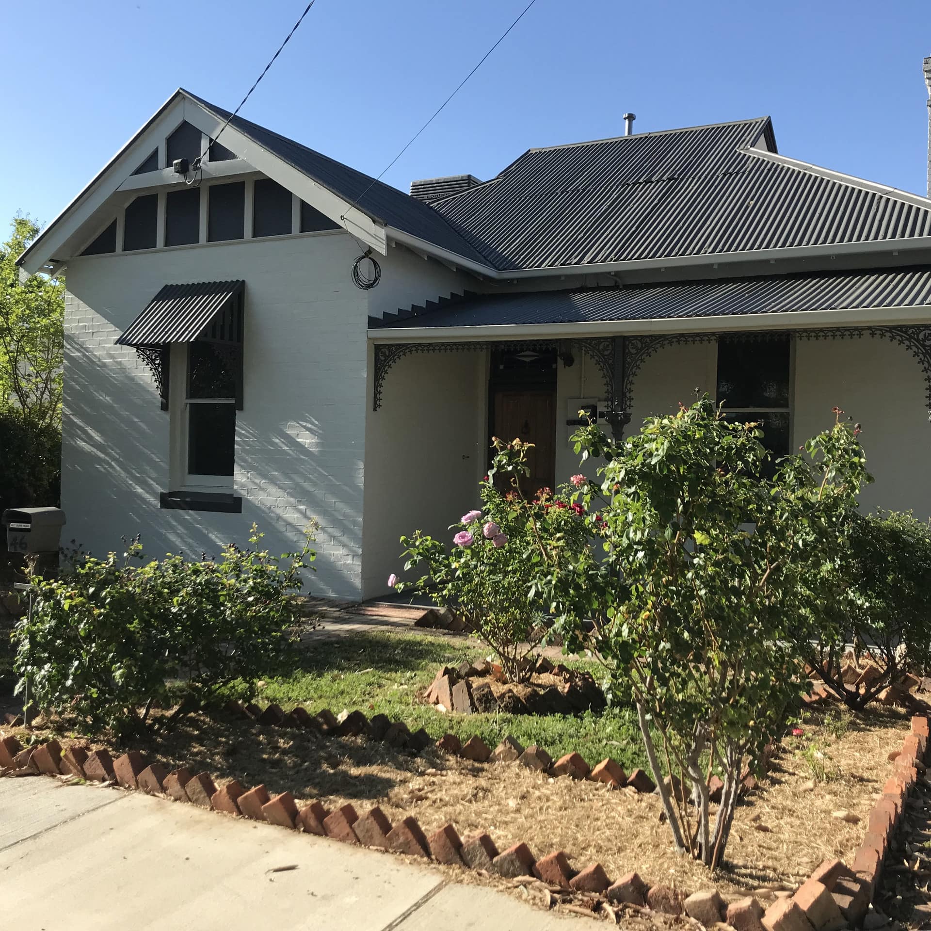 Charming white cottage with black trim, covered front porch, landscaped garden.