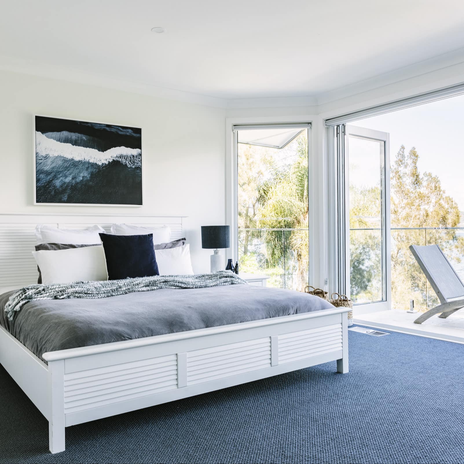 Bedroom with open folding glass doors to balcony with ocean views, a king size bed, black and white furnishings.