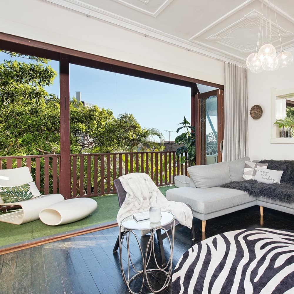 Open living room with black wood floors, a grey sectional, zebra print rug, and folding glass doors to attached balcony.