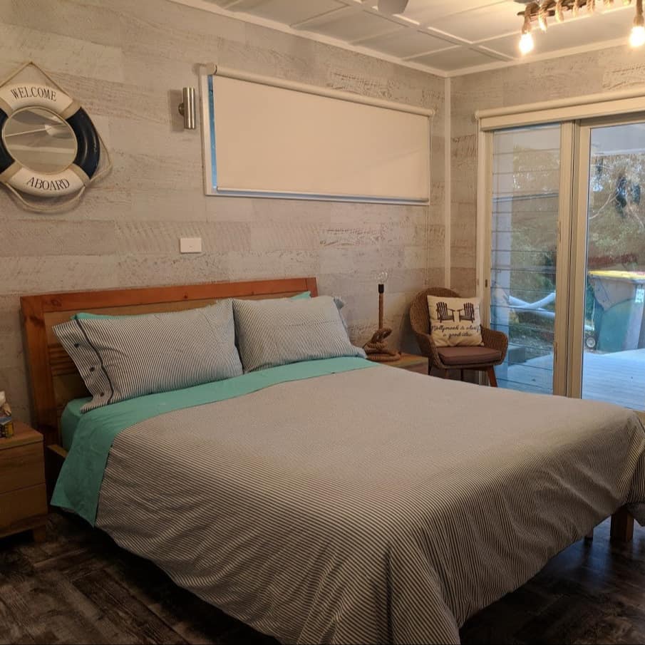 Lovely queen bed in nautical-themed bedroom with whitewashed wood walls and wood-look flooring with view of deck