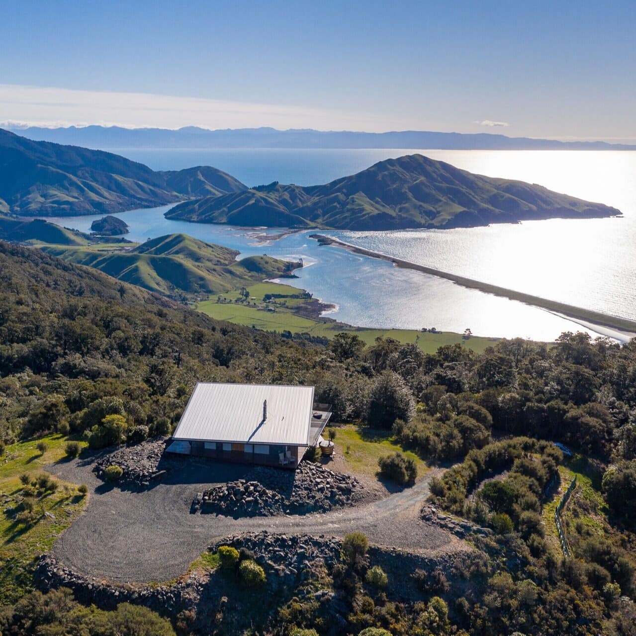 Aerial view of a luxury rental home among trees with the sparkling bay waters and mountains in the distance