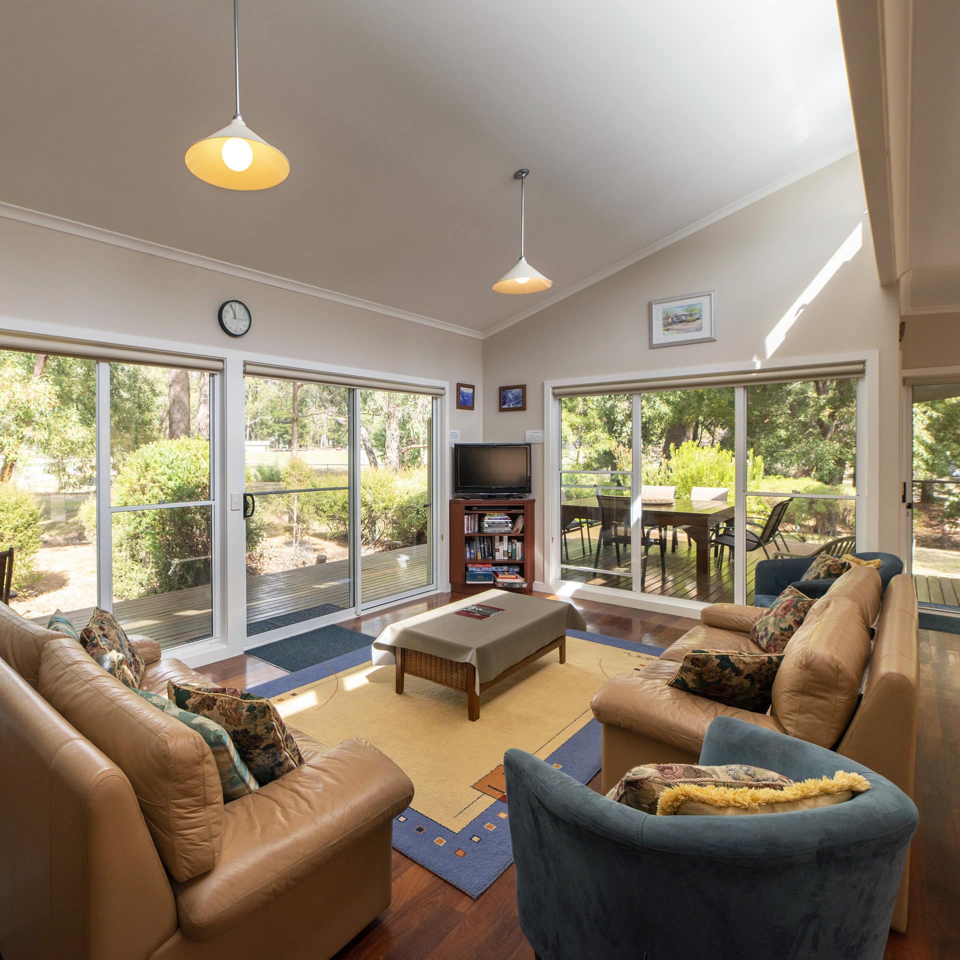 Open living room with hardwood floors, brown leather sofas, tan area rug, blue chairs, and wide windows.