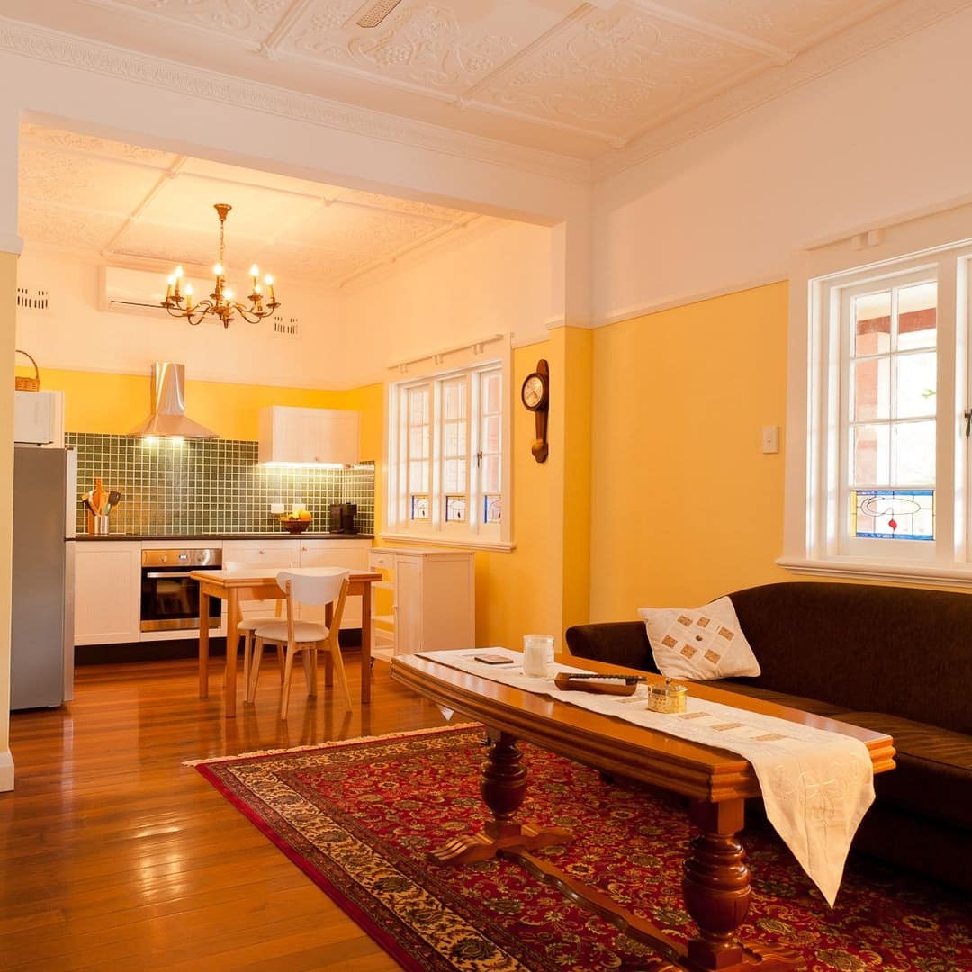 Warm and inviting open lounge and kitchen space painted yellow with couch, fireplace, TV and high ceilings